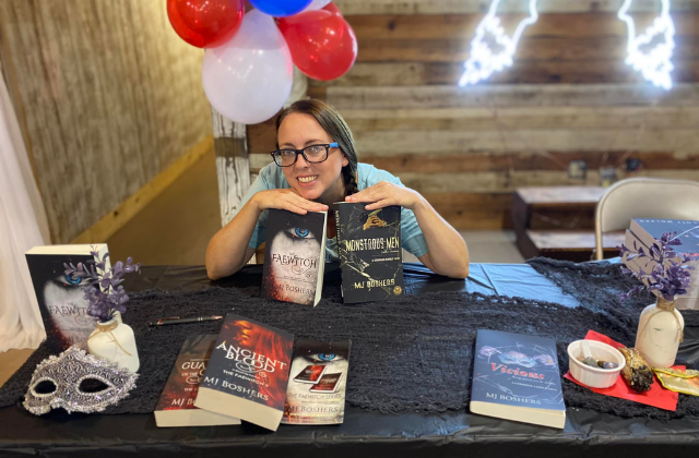 A photo of Marti sitting at a table surrounded by her books for a book signing