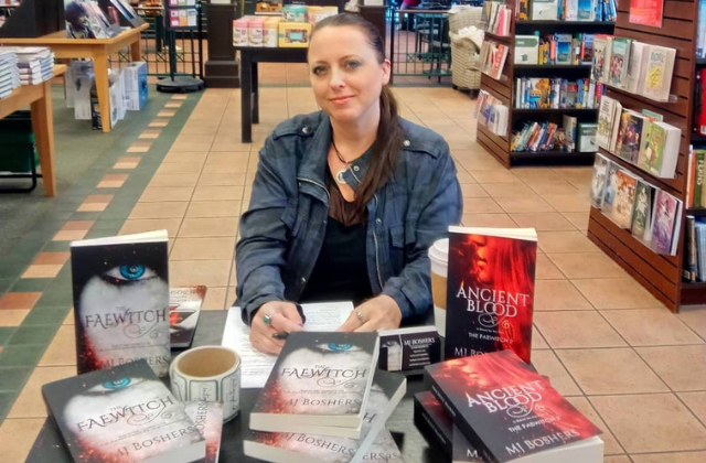 A photo of Marti sitting at a table surrounded by her books for a book signing at Barnes & Noble