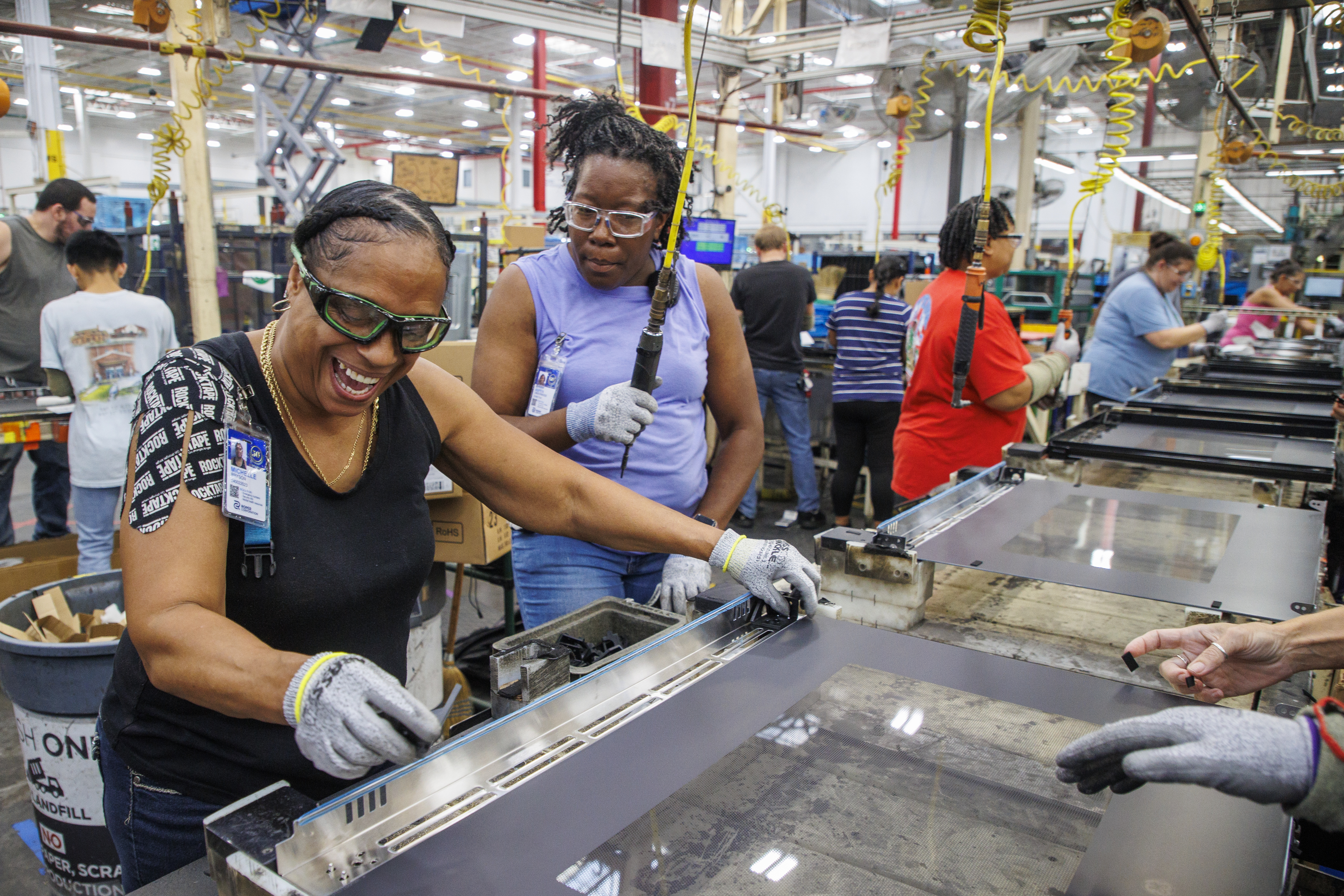 Two women smile as they work on the assembly line