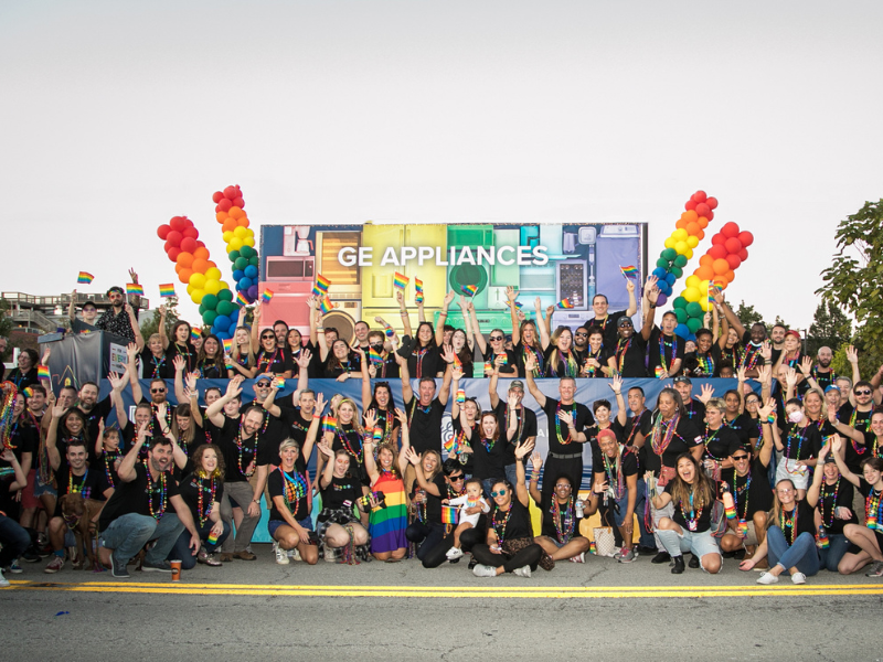Group of men and women wave rainbow flags in front of GEA rainbow float